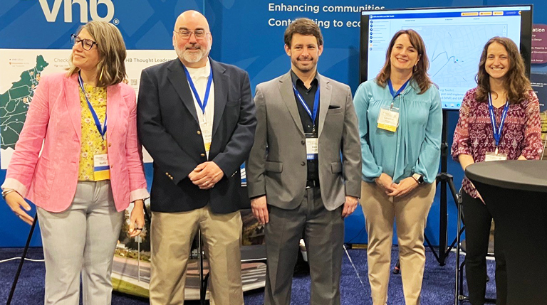 Five professionals standing at a VHB exhibition booth at a conference.