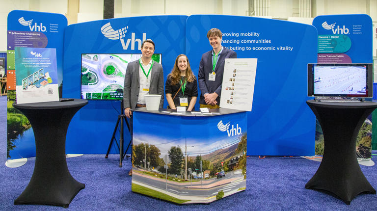  Alex Shulz, Kelsey Munns, and Connor Mountain stand in front of a display at a conference.