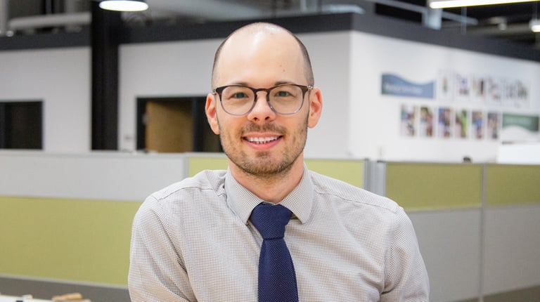 Donny Goris-Kolb in glasses and a button down shirt, leaning on a desk.