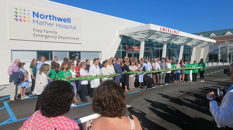 People cutting green ribbon in front of building.