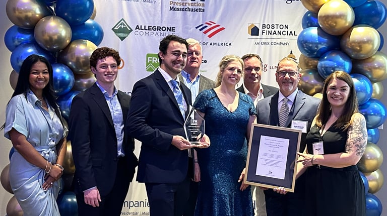 Group of people posing with an award at an event sponsored by WinnCompanies and others, standing in front of a balloon backdrop with company logos.