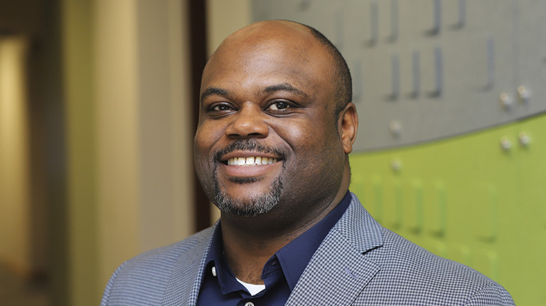 Brandon McAdams smiles at the camera wearing a plaid blazer.