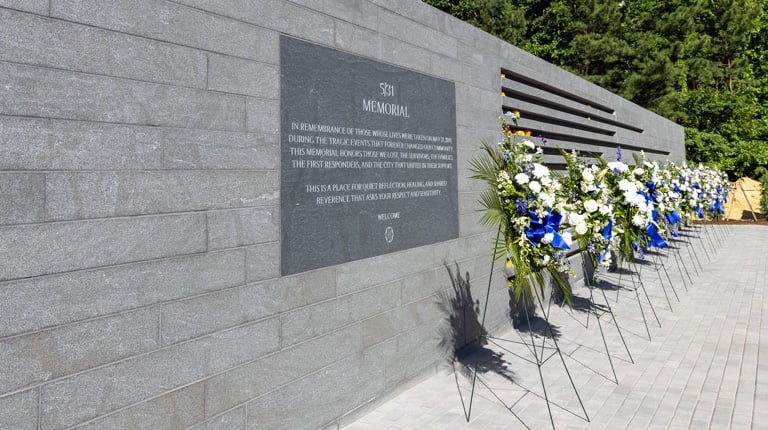 The gray stone memorial is lined with multiple blue floral arrangements.