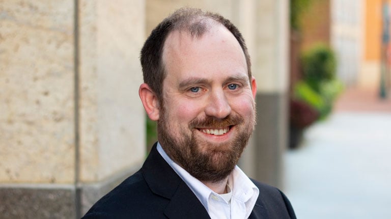 Professional headshot of Michael Lowder wearing business casual attire while smiling outside. 