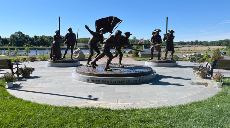 Outdoor monument titled "Freedom's Battleground," featuring bronze statues of soldiers and a woman arranged on circular stone platforms.