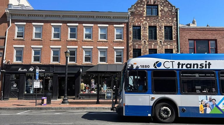 A blue-and-white CTtransit bus at a bus stop in front of a brick building.