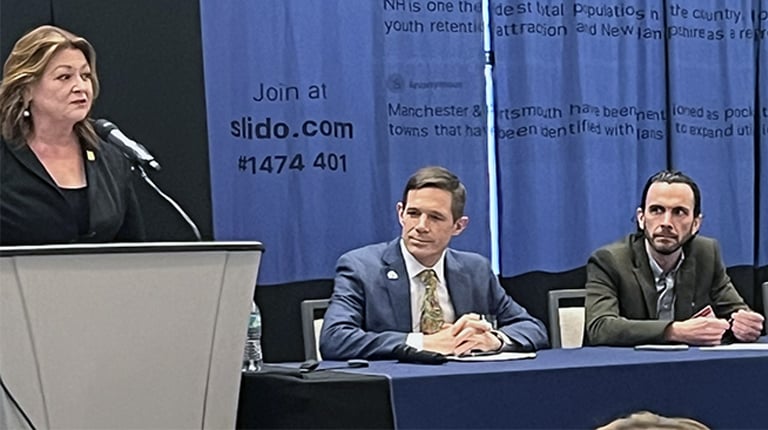 Panelist on four-person panel with moderator speaking to audience.