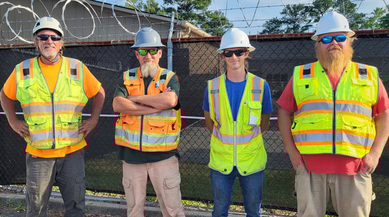 Four men stand together in safety vests preparing to perform rail survey.
