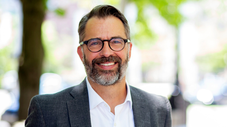 Marc Hustad wears glasses and a suit in an office setting. 