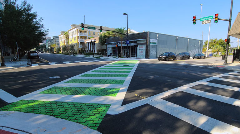 A bicycle crosswalk is painted bright green across a busy intersection.