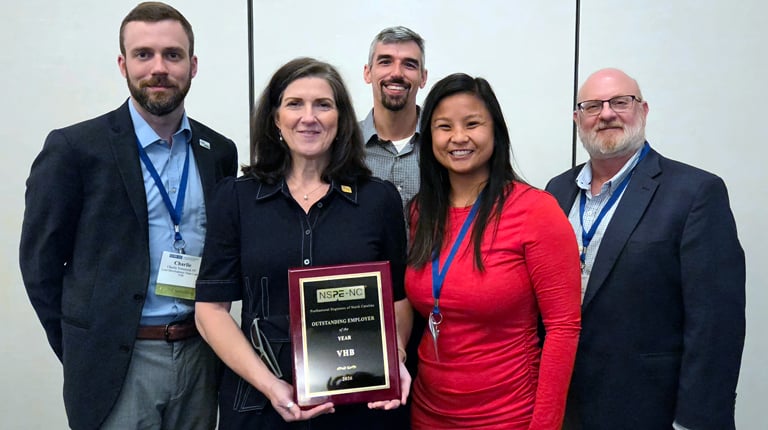 Five people stand side by side and pose for group photo, person in center holds award.