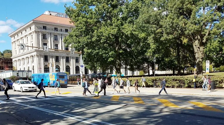 Students cross the street on a crosswalk with a bus in the background