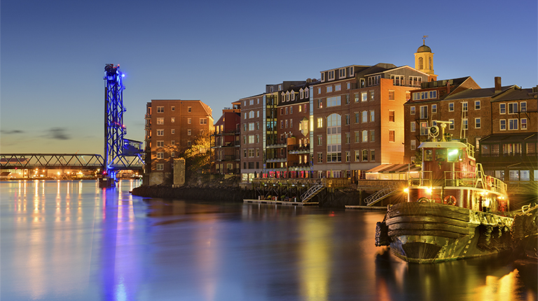 Tugboats on the water at sunset with brick buildings and bridge.