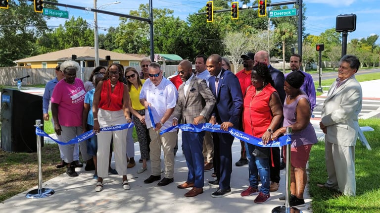 A group of people behind a blue ribbon cutting ceremony on a path.