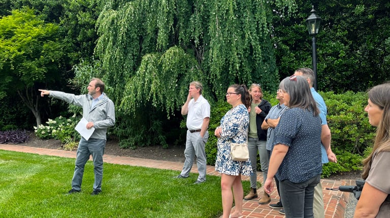 Phillip pointing to landscape features on the green grass next to attendees. 