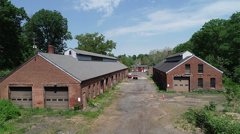 Two vacant industrial buildings surrounded by woods.