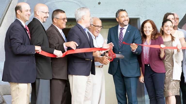 People smiling while cutting red ribbon