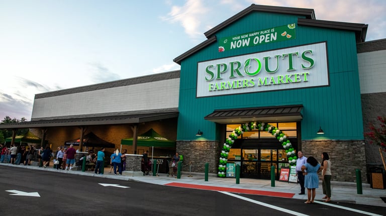 New green building with a large Sprouts sign and a balloon arch surrounding the entryway.