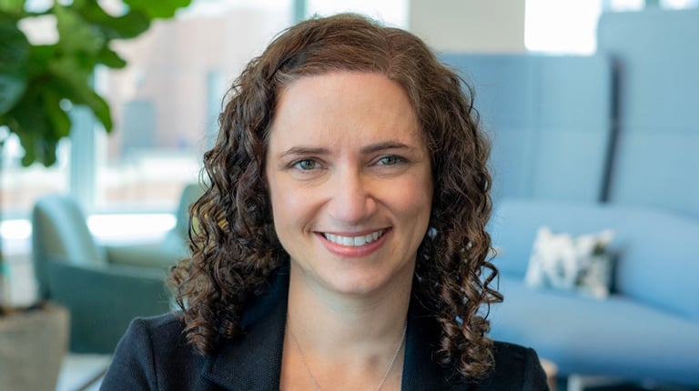 A smiling woman with curly brown hair in a black blazer.