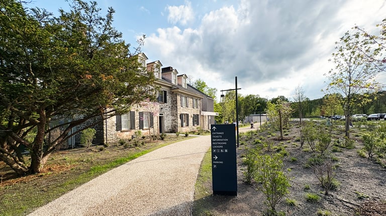 Pathway to building surrounded by greenery and a directional sign.