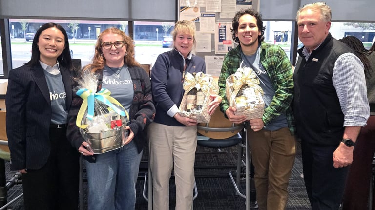 A group of people standing indoors holding wrapped gift baskets during auction event.