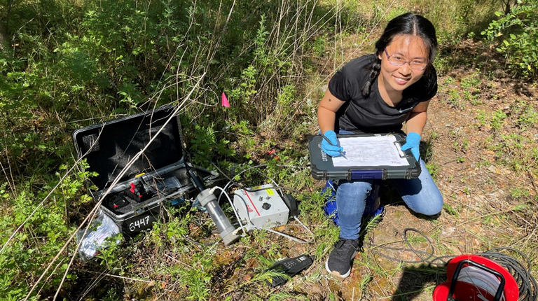 VHB intern kneeling on the ground holding a tablet and using groundwater sampling equipment
