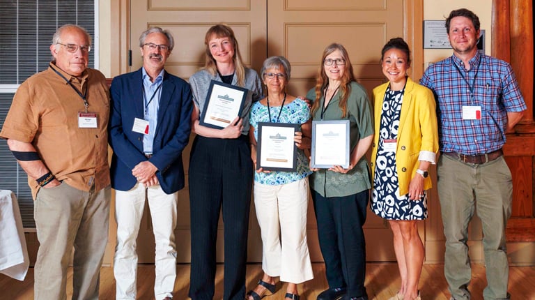 Group of people posing with awards at an event, standing in front of double doors.