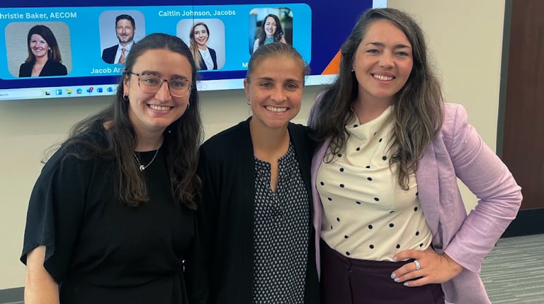 Three individuals smiling in front of a presentation screen at a WTS (Women's Transportation Seminar) event.
