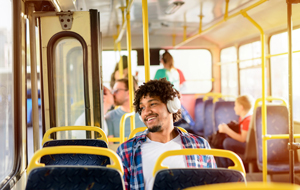 A man is seated on a bus with headphones on looking out the window.