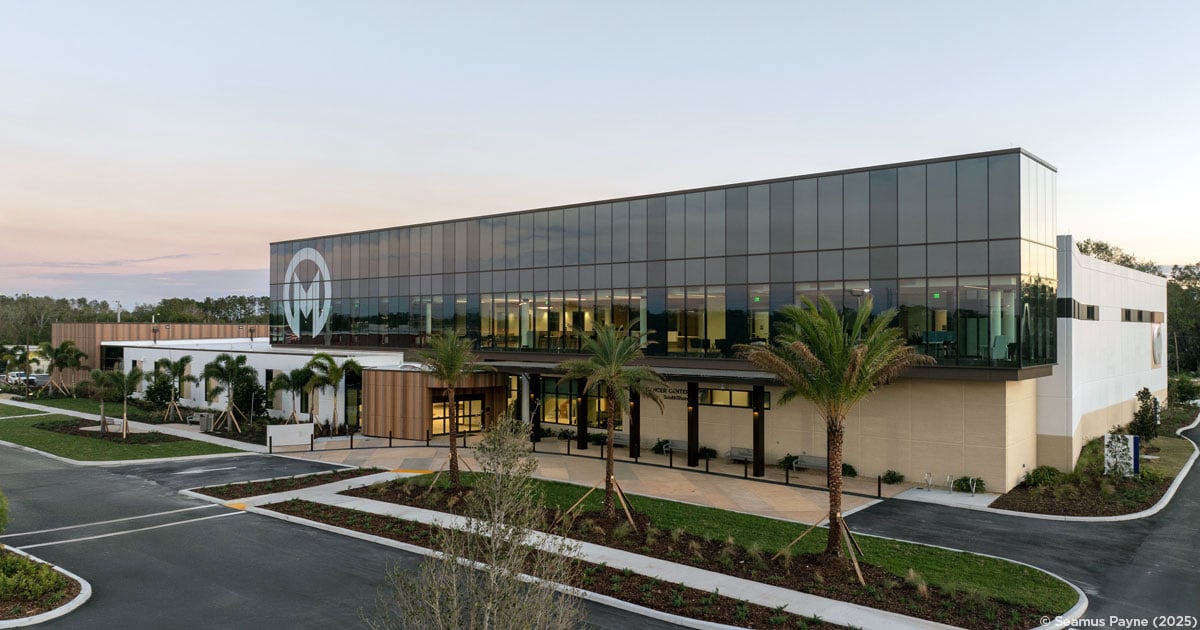A modern healthcare facility in the evening with palm trees in front.