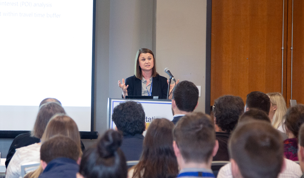 A person stands at a podium speaking to a seated audience.  