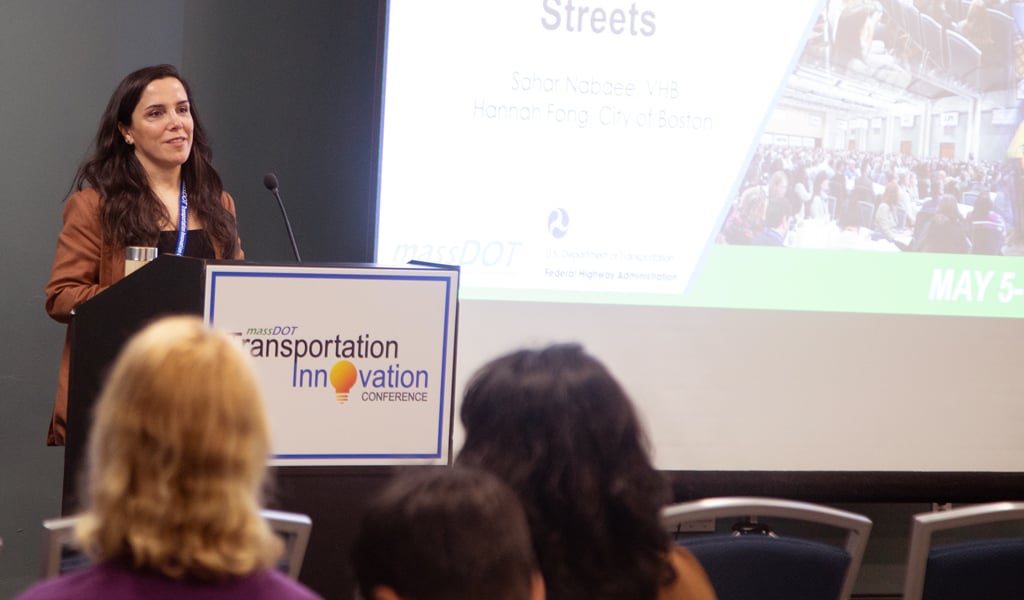 A person stands at a podium speaking to a seated audience.  