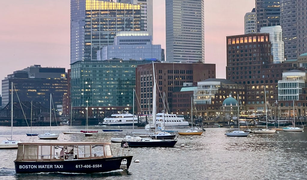 A Boston Water Taxi moves across a harbor, surrounded by several sailboats.