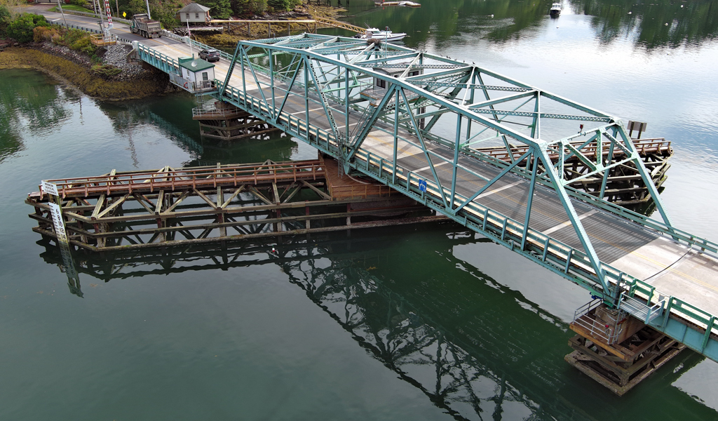 Bridge over water with a wooden fender system and teal truss.