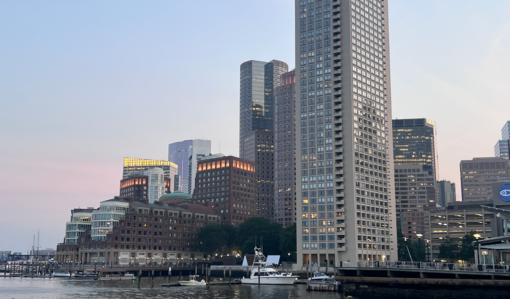 Skyline of Boston featuring tall buildings at dusk, reflected in the water.