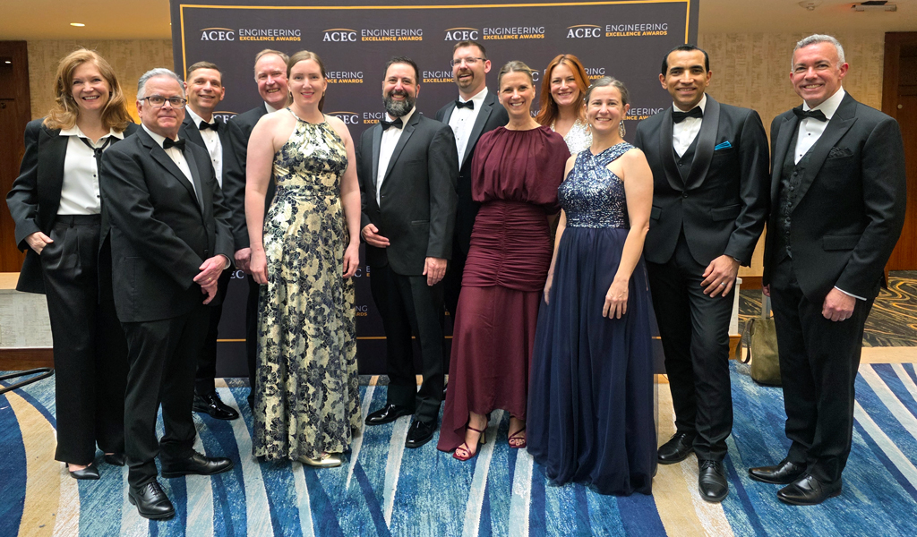 A group of 12 people dressed in black tie attire at an awards ceremony. 
