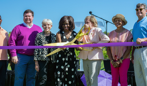 A smiling group of people hold a big pair of scissors for a ribbon cutting