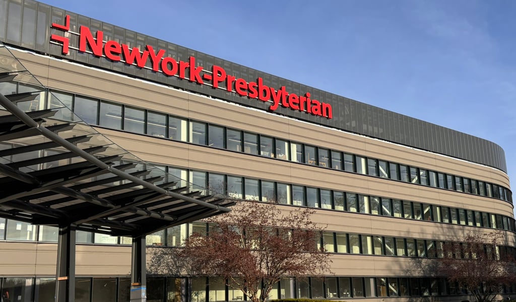 Exterior view of NewYork-Presbyterian&rsquo;s The One outpatient facility with building signage, covered entry canopy, and campus circulation area.