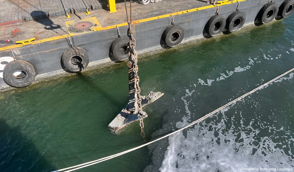 Anchor being pulled out of the water onto a large ship with heavy machinery.
