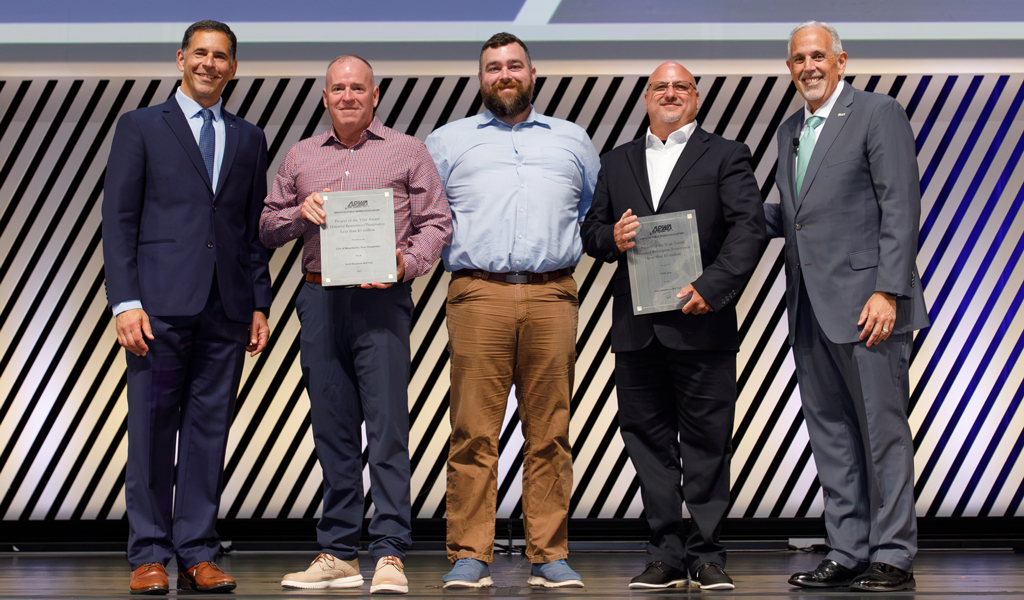 Five individuals are standing on a stage at a professional event, each holding a certificate, smiling, and dressed in business attire.