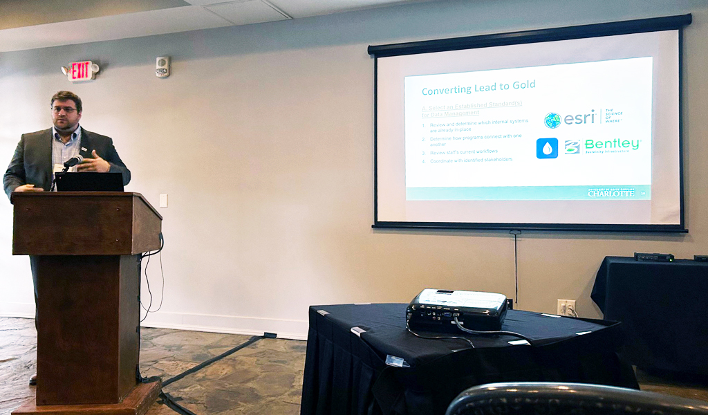 Craig presenting at the podium with his slide projected on a screen beside him.