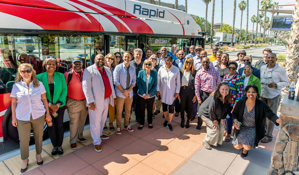 A group of people stand outside a rapid transit bus on a San Diego street.