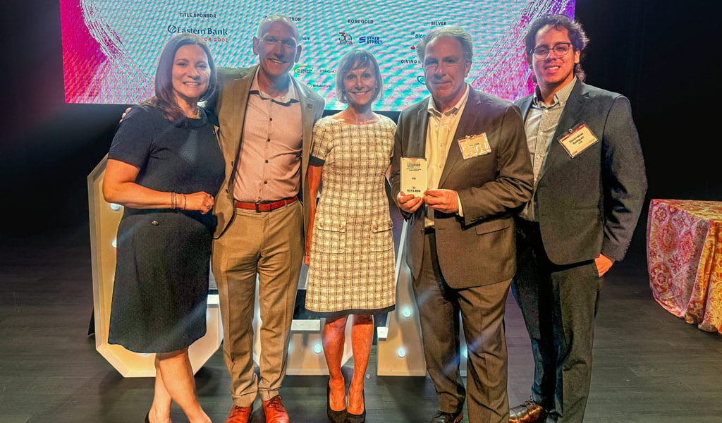 A group of five people smiling in front of a sign that reads "Corporate Citizenship Awards" from the Boston Business Journal. They are dressed in formal attire.