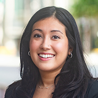 A person with long, dark hair wearing a white top and a black jacket.