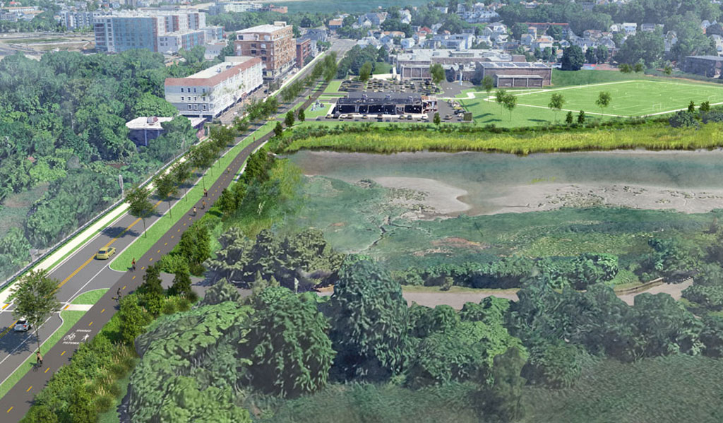 An aerial view of a marshy area and a sports field, showcasing a winding road lined with trees, nearby modern buildings, and expansive green spaces.