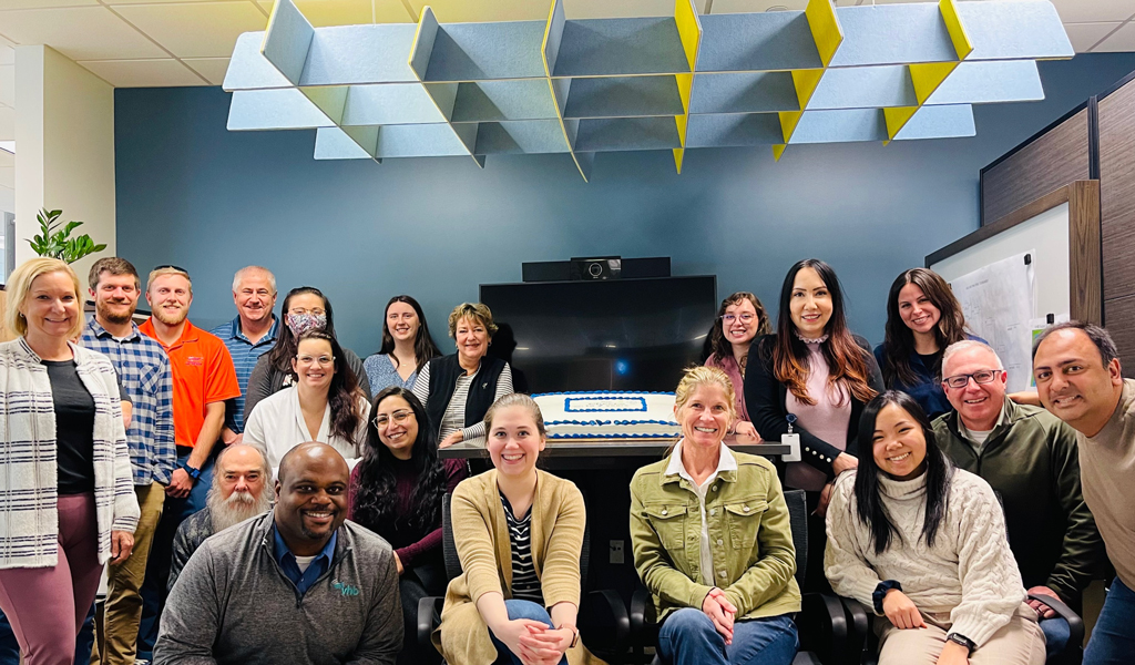 Members of the Virginia Beach office smile at the camera with their cake. 