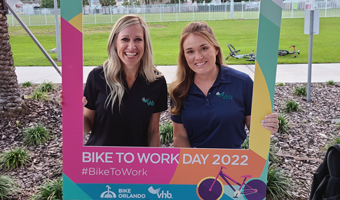 Jennifer Rader and Gabbi Grimaldi stand behind a selfie frame from bike to work day 2022