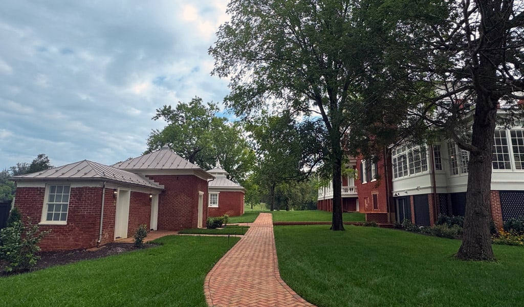 Brick walkway running through a landscaped lawn between historic brick buildings and the side of Birdwood Mansion.