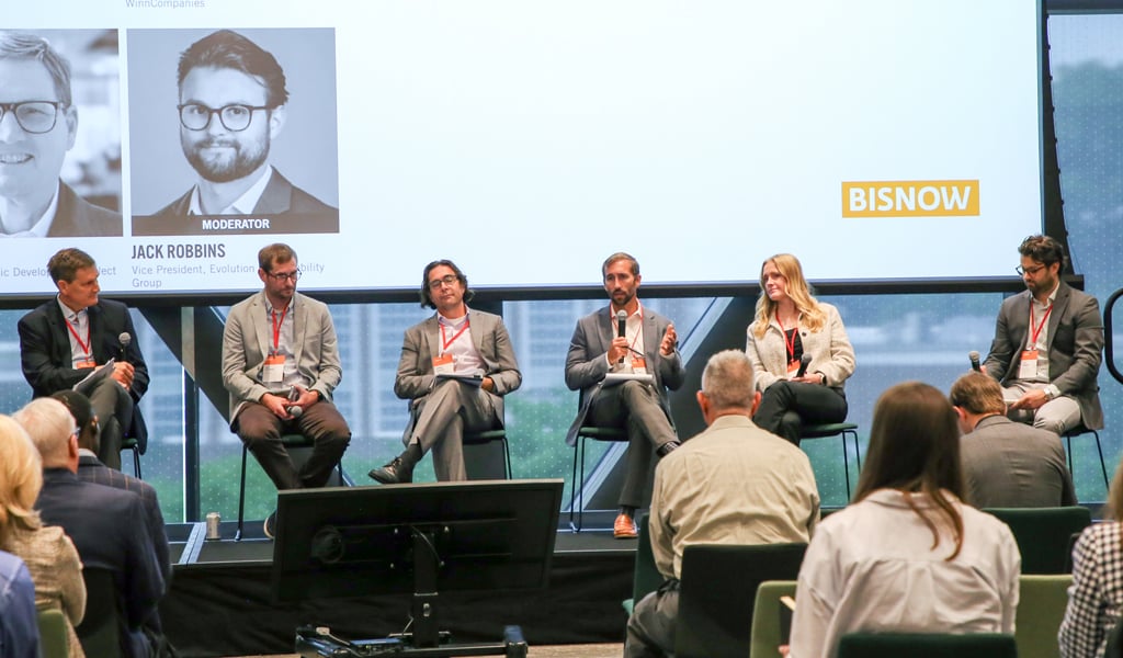 A panel of six people sitting on chairs on a stage at a Bisnow event.