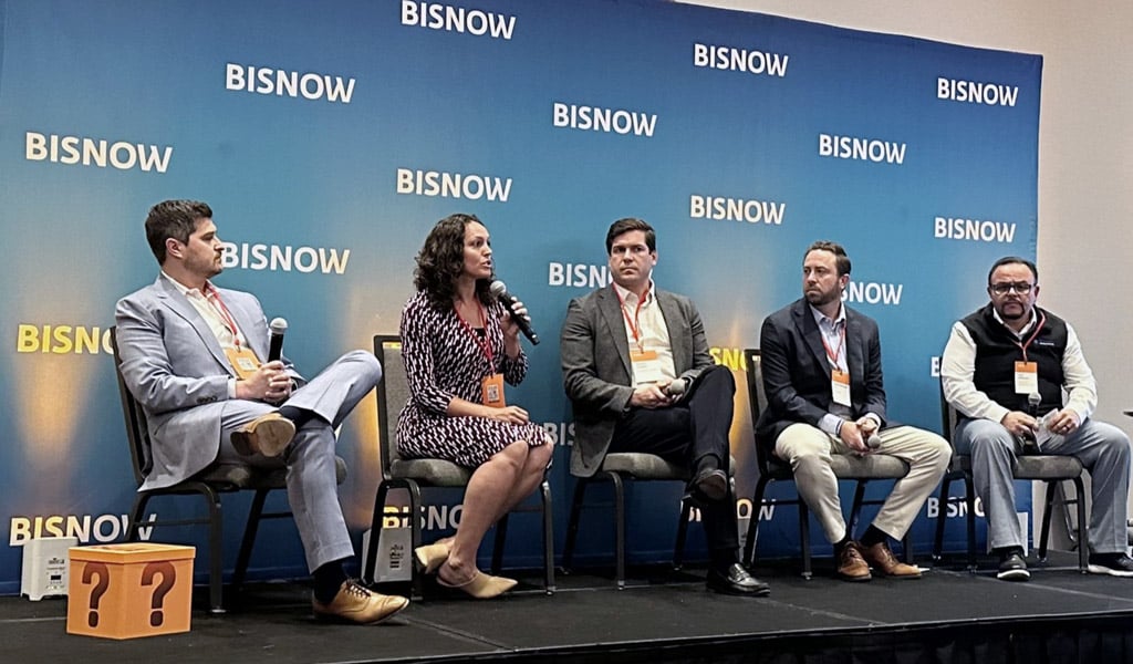 A panel of five individuals seated on stage in front of a "Bisnow" backdrop, engaging in discussion.